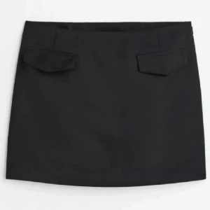 Svart kortkjol med fickdetaljer - Snygg svart minikjol med raka linjer och två fickdetaljer framtill. Kjolen har en enkel och stilren design som är lätt att matcha med olika toppar. Passformen är normal och kjolen sitter högt i midjan för en modern look.