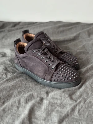 Mörkgrå Christian Louboutin sneakers - Snygga mörkgrå sneakers från Christian Louboutin, storlek 43, några spikar borta på ena skon då jag spelat lite fotboll med dem. Säljs billigt eller byte mot andra skor, tveka inte med att höra av er😻(400kr om du kan hämta dem i Vadstena)