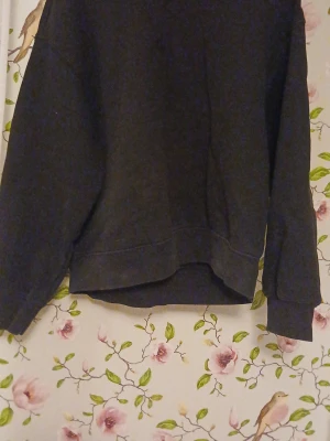 Svart basic sweatshirt - En enkel svart sweatshirt med rund hals och långa ärmar. Tröjan har en avslappnad passform och ribbade muddar vid ärmslut och nederkant. Perfekt för en casual look och lätt att matcha med andra plagg.