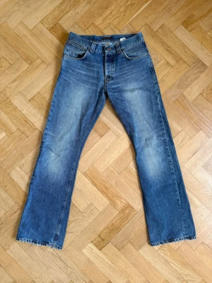 Nudie Jeans, Regular Ralf - Klassiska blå jeans från Nudie Jeans med rak passform och slitna detaljer. Jeansen har fem fickor, knappgylf och ljusa tvättade partier på framsidan och baksidan. Tillverkade i bomull för en skön känsla och tidlös look.  W32 L34📐  Waist: 41cm Length: 112cm Leg opening: 24cm