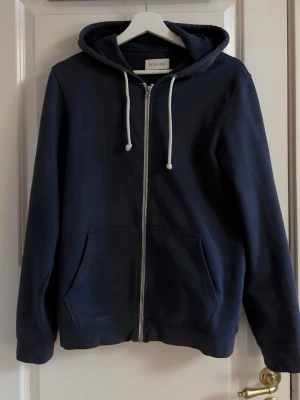Mörkblå zip hoodie från PIER ONE - Mörkblå hoodie med dragkedja från PIER ONE. Klassisk modell med huva och vita dragsnören, samt två stora fickor framtill. Perfekt för en avslappnad och stilren look.