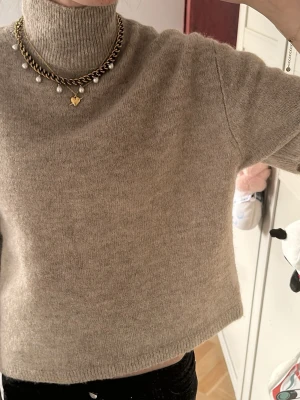 Beige stickad polotröja kort modell - Mysig beige stickad polotröja i kortare modell med halvlånga ärmar. Tröjan har en hög krage och är tillverkad i ett mjukt, ull-liknande material. Perfekt för lager på lager och enkel att styla till olika outfits.