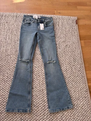 Ljusblå bootcut jeans från Lager 157 - Säljer ett par ljusblå bootcut jeans från Lager 157 med slitningar vid knäna. Byxorna är helt nya och säljer dom endast för att det var fel storlek och inte gick att returnera.