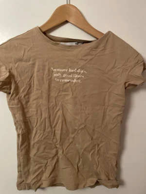 Beige t-shirt med texttryck - Säljer en beige t-shirt från lager 157  med vit text på bröstet: 'No more bad days, only good times to remember.' T-shirten har rund halsringning och korta ärmar. Perfekt för en avslappnad och trendig look.