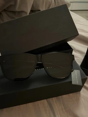 Svarta solglasögon från Daniel Wellington, helt nya  - Snygga svarta solglasögon från Daniel Wellington med rektangulär form och stilren design. Glasögonen har mörka linser och bågar i plast som ger en modern och clean look. Perfekta för dig som vill ha en klassisk accessoar med edge. Helt nya aldrig använda! Nypris är 1200kr. Kan gå ner i pris till ca 700-600kr vid snabbt köp 