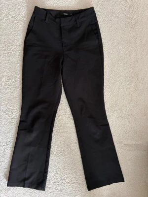 Svarta kostymbyxor från Bik Bok - Snygga svarta kostymbyxor från Bik Bok med raka ben och klassisk passform. Byxorna har hällor för skärp, sidofickor och är tillverkade i ett mjukt, vävt material som ger en stilren look.