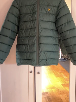 Grön pufferjacka från Lyle & Scott - Snygg grön pufferjacka från Lyle & Scott med gul logga på bröstet. Perfekt nu till våren då den inte är så tjockt materiel. Använder inte jackan längre då den är för liten. Pris går diskutera. 