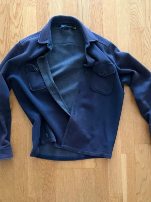 RalphLauren Overshirt, Marinblå - Snygg mörkblå overshirt i mjuk fleece med klassisk krage och två bröstfickor med lock och knapp. Perfekt lager-på-lager-plagg med knäppning framtill och avslappnad passform. Passar dig som gillar enkel och stilren look.