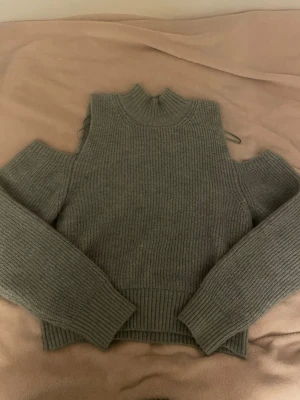 Grå tröja med cut out från Gina Tricot - Trendig grå stickad tröja från Gina Tricot med cut out-detaljer på axlarna och ribbad krage. Tröjan har långa ärmar och är gjord i mjukt, ribbstickat material. Skriv för frågor!