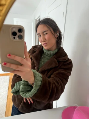 Mörkbrun pälsjacka med krage - Snygg mörkbrun pälsjacka med bred krage och klassisk passform. Jackan har en mjuk och fluffig yta som ger en lyxig känsla. Perfekt för kalla vinterdagar och enkel att matcha med olika outfits.