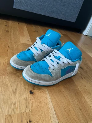 Turkosa Air Jordan 1 Low sneakers - Säljer ett par Air Jordan 1 Low sneakers i turkos och grå mocka med vita skosnören och vit sula. Ikoniska Jumpman-loggan på plösen och klassisk låg siluett. Perfekta för dig som vill sticka ut med färg och stil.