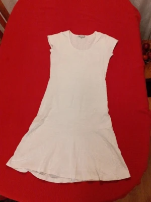 Vit kortärmad klänning med mönster - Säljer en vit kortklänning med diskret invävt mönster. Klänningen har rund halsringning och korta ärmar. Materialet känns mjukt och lätt, perfekt för varmare dagar. Enkel och stilren design som är lätt att matcha.