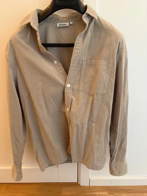 Beige manchesterskjorta från Weekday - Säljer en beige manchesterskjorta från Weekday med klassisk krage, bröstficka och knäppning framtill. Skjortan har lång ärm och en avslappnad passform som passar perfekt till jeans eller chinos.