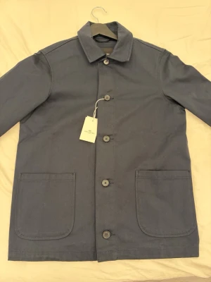 Mörkblå overshirt från John Henric - Stilren mörkblå overshirt från John Henric. Klassisk rak passform med stora utanpåfickor framtill och knäppning med fem knappar. Långa ärmar med dubbla knappar vid manschetten och enkel krage för en clean look. Den är helt ny och är aldrig använd!✅Priset är inte hugget i sten 🪨🔨