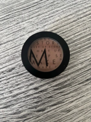 Brun ögonskugga Make Up Store - Säljer en rund ögonskugga från Make Up Store i en varm brun nyans. Kommer i en svart plastförpackning med genomskinligt lock där loggan syns tydligt. Perfekt för att skapa naturliga eller djupare ögonlooks.