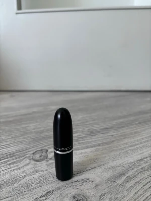 MAC läppstift i nude-rosa nyans - MAC läppstift med klassisk svart hylsa och silverdetalj. Färgen är en snygg nude-rosa ton som passar perfekt till en naturlig look. Läppstiftet har en rundad form och känns lyxigt med sin ikoniska design.