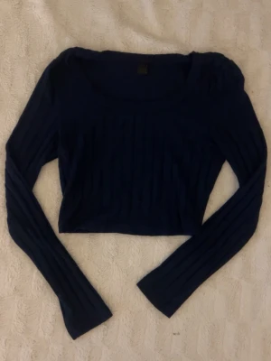 mörkblå croppad ribbad topp -  mörkblå croppad topp med långa ärmar och rund halsringning. Toppen är ribbad vilket ger en trendig och bekväm känsla.