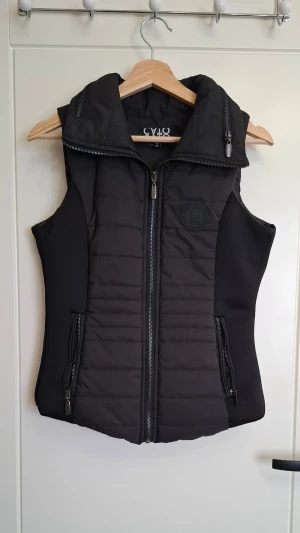 Svart väst från Cato - Snygg svart dunväst från Cato. Västen har två dragkedjefickor framtill och en diskret logotyp på bröstet. 