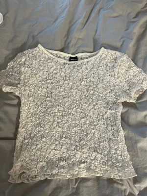 Vit spetsblus med kort ärm - Säljer en söt vit blus med korta ärmar och blommig spets över hela toppen. Perfekt för dig som vill ha en luftig och lätt topp till sommaren. Rund halsringning och transparent känsla.