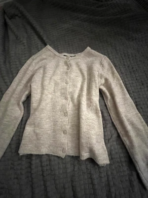 Ljusgrå basic kofta med knappar - En enkel och stilren ljusgrå kofta med rund halsringning och knäppning framtill. Koftan har långa ärmar och är tillverkad i ett mjukt, stickat material.