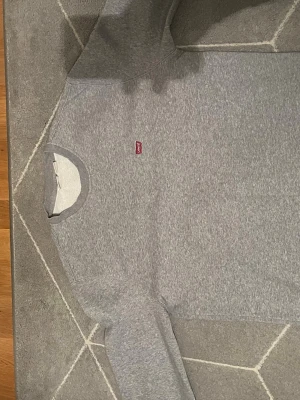 Grå sweatshirt från Levi's - Klassisk grå sweatshirt från Levi's med rund halsringning och liten röd logotyp på bröstet. Tröjan har ribbade muddar vid ärmslut och nederkant. Perfekt för en stilren look. Perfekt till våren!