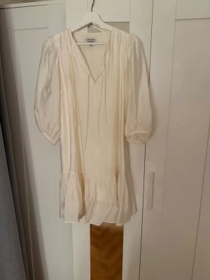 Vit kort klänning från & other stories  - Supersöt vit kort klänning från By Malina med puffärmar, v-ringning och knytband framtill. Klänningen har volang nertill och är tillverkad i ett lätt och luftigt material som passar perfekt till varmare dagar. Säljer då den inte kommer till användning, endast använd ett fåtal gånger! Skriv vid frågor💗