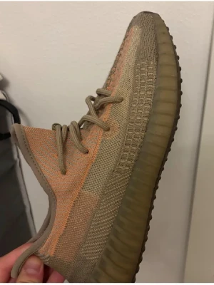 Yeezy Boost 350 V2 Earth sneakers - Snygga Yeezy Boost 350 V2 Earth sneakers med beige och bruna toner samt en orange stripe på sidan. Ovandelen är i stickad mesh och sulan är tjock och ribbad i gummi. Perfekta för dig som gillar streetwear och vill sticka ut.