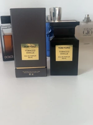 Tom Ford Tobacco Vanille EdP 100ml - Tom Ford Tobacco Vanille Eau de Parfum 100 ml med lyxig svart glasflaska och guldfärgad etikett. Doften kombinerar varma toner av tobak och vanilj. Flaskan har en elegant, fyrkantig form och levereras med originalförpackning. Pris kan diskuteras vid snabb affär.