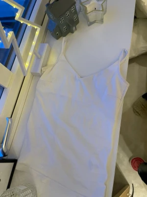 Vit linnetopp från lager 157 - Säljer en enkel och stilren vit linnetopp från 152. Toppen har smala axelband och ärmlös design, perfekt för varma dagar eller som lager under andra plagg. Tillverkad i mjuk bomull för skön känsla och bra passform. V ringat vitt linne från lager 157 i storlek zs, säljer två st av dessa vita även ett svart om någon så vill köpa