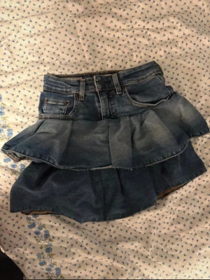 Volangkjol i denim från Levi's - Säljer en blå jeanskjol från Levi's med volangdetaljer och klassisk femficksdesign. Kjolen har en kort modell och är tillverkad i slitstarkt bomullsdenim. Perfekt för dig som gillar en avslappnad men trendig stil. omsydd från bootcut jeans till volangkjol! priset kan diskuteras köpta för 1200kr