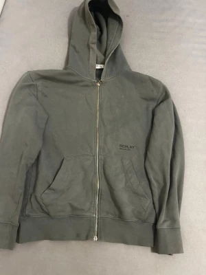 Grön zip-hoodie från Replay - Snygg grå hoodie med dragkedja från Replay. Klassisk modell med huva och två stora fickor framtill. Diskret Replay-logga på bröstet. Perfekt för en avslappnad och cool stil. Tillverkad i mjukt bomullsmaterial.