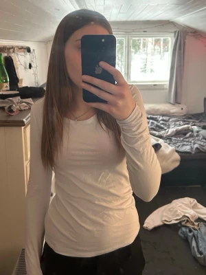 Vit långärmad topp med v-ringning - En enkel och stilren vit långärmad topp med v-ringad hals. Sitter tight och är gjord i mjukt bomullsmaterial som känns skönt mot huden. Perfekt att matcha med jeans eller kjol för en clean look.