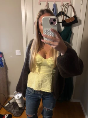 Gul topp med rynkade detaljer - Snygg gul topp med rynkade detaljer och smala axelband. Toppen har en feminin v-ringning och figurnära passform, perfekt för att lyfta en enkel outfit. Materialet ser ut att vara mjukt och lätt, vilket gör den bekväm att bära.