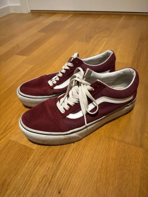 Vinröda Vans Old Skool sneakers - Vinröda Vans Old Skool sneakers med vit sula och klassisk vit sidostripe. Ovandelen är i mocka och canvas, med vita skosnören och detaljer. Perfekta för dig som gillar en retro och street-inspirerad stil.