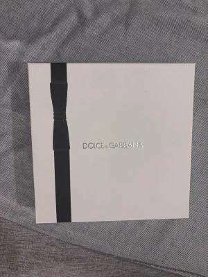 Dolce & Gabbana K parfymset - 1 av 10 bästa parfymerna enligt kicks lista för herrar framröstad, jättegod men jag har två för köpte fel så säljer en för trodde det var den andra men bara öppnat och testat två sprut. Se bild. Snyggt parfymset från Dolce & Gabbana med doften K. Setet innehåller en blå glasflaska parfym med gulddetaljer, en matchande mörkblå tub och en mörkblå deodorantstick. Allt levereras i en elegant vit presentask med svart band och logga.