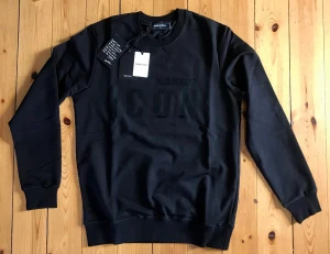 Svart sweatshirt från Dsquared2 ICON - Svart sweatshirt från Dsquared2 med stor, svartglänsande 'ICON'-text på bröstet. Rund halsringning, ribbade muddar och avslut. Tillverkad i mjuk bomullsblandning. Perfekt för en trendig streetwear-look.