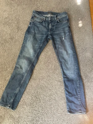 Nudie Jeans - Snygga blå jeans från Nudie Jeans med klassisk femficksdesign och raka ben. Jeansen har en lätt tvättad look med slitningar och detaljerade sömmar på bakfickorna. Tillverkade i bomull för en skön och avslappnad känsla.