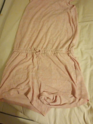 Ljusrosa jumpsuit från H&M - Supersöt ljusrosa jumpsuit från H&M med korta ben och resår i midjan. Tillverkad i mjukt och bekvämt material, perfekt för en avslappnad stil. Dragsko i midjan för extra passform och två sidofickor. Enkel och stilren design.