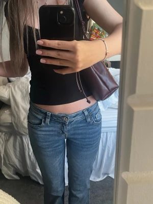 Blå low waist bootcut jeans - Säljer ett par blå low waist jeans med bootcut-modell. Jeansen har klassiska fem fickor, ljus tvätt och raka ben. Storlek 34 skulle passa nog 36 också💗