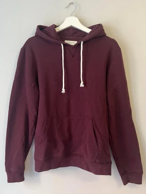 Vinröd hoodie från Pier One - Snygg vinröd hoodie från Pier One med klassisk känguruficka och vita dragsnören i huvan. Hoodien har en avslappnad passform och är tillverkad i mjukt bomullsmaterial. Perfekt för en chill och stilren look.