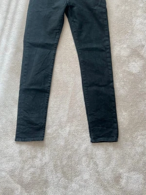 Svarta skinny jeans från Levi's - Svarta skinny jeans från Levi's med klassisk femficksdesign och röd Levi's-tagg på bakfickan. Jeansen har smal passform och är tillverkade i stretchigt denimtyg. Knappt använda. W30 L32