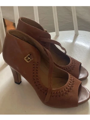 Bruna Clarks klackar  - Superfina bruna klackar från kvalitetsmärket Clarks i storlek 39! Bekväm passform med fin flätad detalj och ankelrem. Gjorda i äkta läder, så de håller toppkvalitet. Jättefint skick, säljes för 399 kr (nypris ca 1100 kr).