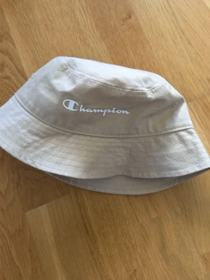 Beige bucket hat från Champion - Snygg beige bucket hat från Champion med vit broderad logga framtill. 