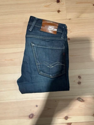 Replay Anbass - Säljer ett par mörkblå jeans från Replay. Jeansen i modellen Anbass som är slim i passformen. De är i väldigt bra skick men har några få slitningar som syns i bilderna. Storlek: W28 L32. Hör gärna av dig vid frågor!