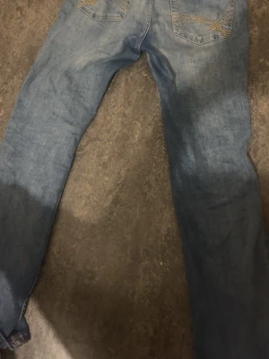 Blå bootcut jeans med broderade fickor - Säljer ett par klassiska blå bootcut jeans med snygga broderade detaljer på bakfickorna. Jeansen har en lätt tvättad look och är låg midjade.
