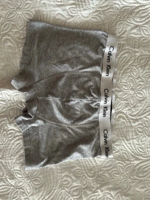Grå boxerkalsonger från Calvin Klein - Snygga grå boxerkalsonger från Calvin Klein med vit resår och svart logotyp runt midjan. Klassisk passform och mjukt material som sitter skönt hela dagen. Perfekta för dig som gillar stilrena underkläder.