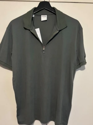 Half zip t-shirt  - Stilren grå t-shirt från Selected Homme med korta ärmar och en ribbad krage. Tröjan har en snygg half zip-dragkedja framtill och är gjord i mjuk bomull. Perfekt för dig som gillar en clean look med lite edge.