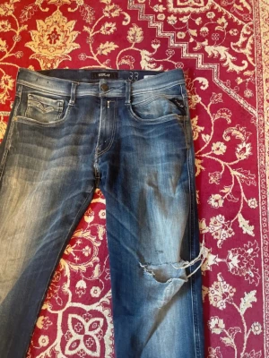 Replay anbass med slitage - Säljer ett par blå jeans från Replay med skinny fit och slitningar på höger ben. Jeansen har klassisk femficksdesign, dragkedjegylf och tydliga tvättade detaljer för en cool look.