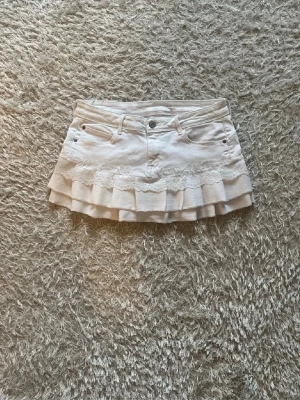 Vit volangkjol med spetsdetaljer - En vit jeanskjol omsydd från ett par jeans. 🌷  Midjemått tvärsöver- ca 38cm  Längd - 29cm