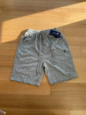 Gråa shorts från Ralph Lauren - 👕 Märke: Polo Ralph Lauren 📏 Storlek: M 🎨 Färg: Grå med svart logga ✨ ☀️ Stilrena och bekväma shorts från Polo Ralph Lauren – perfekta för sommaren. Enkel och tidlös design som passar lika bra till t-shirt som hoodie. Tillverkade i mjukt och skönt material med ikonisk svart logga.  ✨ Skick: Helt nya med tags kvar 🧼 Aldrig använda 👌 Perfekta för både vardag och semester